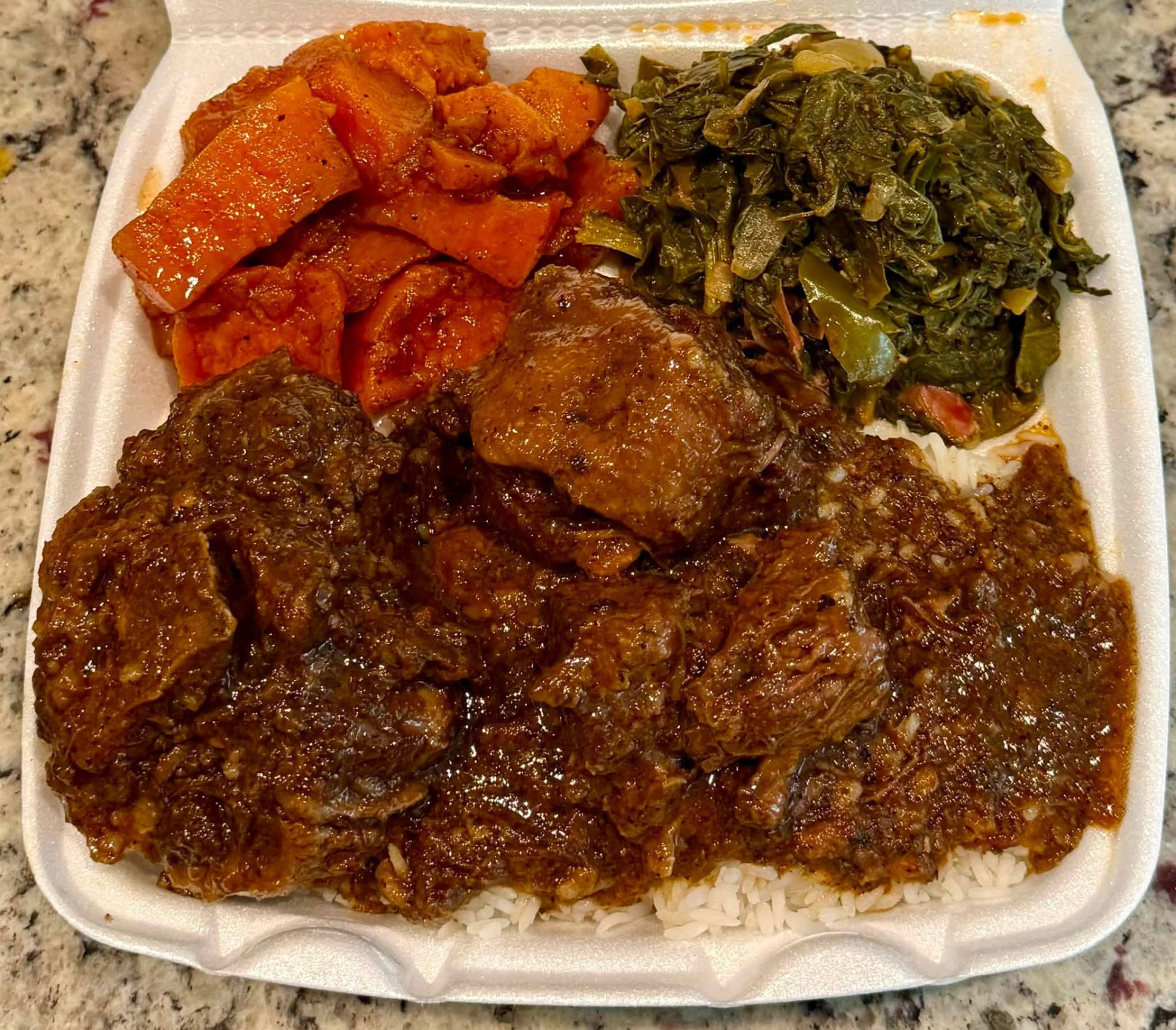 Smothered oxtails plate over rice with candied yams and greens