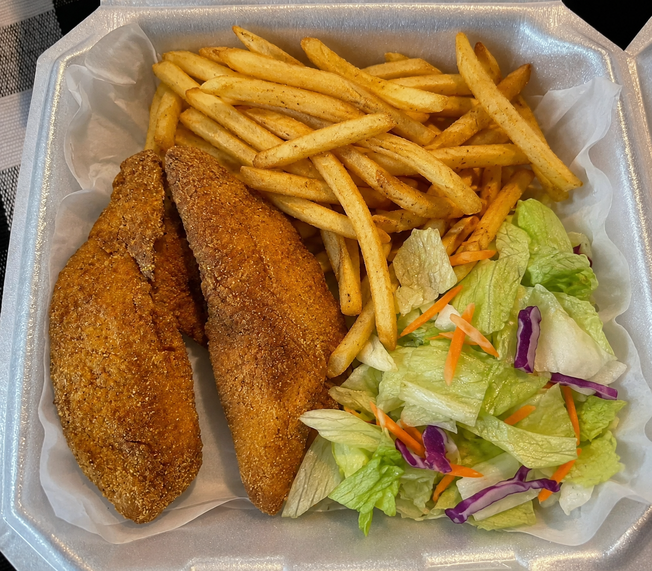 Two fried fish fillets with seasoned fries and a fresh side salad